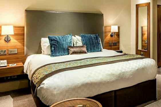 Bilde av et hotellrom med en dobbeltseng, nattbord og garderobe i tre. (AI-generert tekst)