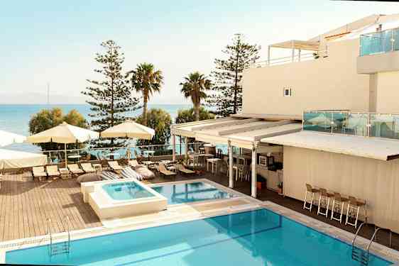 Et hotellområde med et basseng, solsenger og parasoller ved havet. (AI-generert tekst)