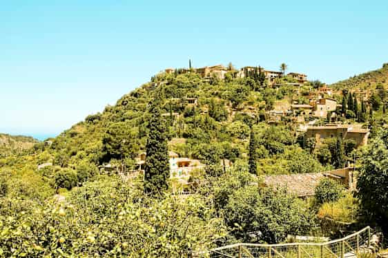 En scene med skrånende landskap fylt med grønn vegetasjon, hus og lave bygninger spredt blant trærne. (AI-generert tekst)