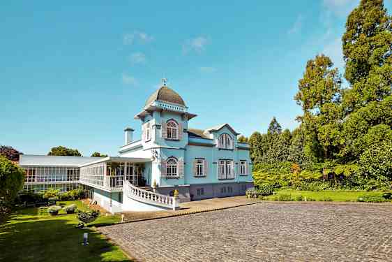 En lyseblå bygning med store vinduer og grønne omgivelser. (AI-generert tekst)