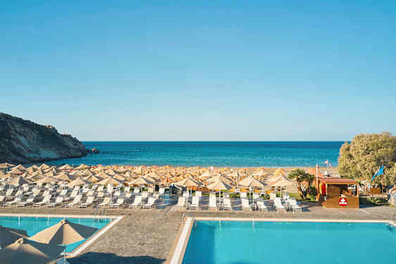 Et basseng foran en strand med solsenger og parasoller, og havet i bakgrunnen. (AI-generert tekst)