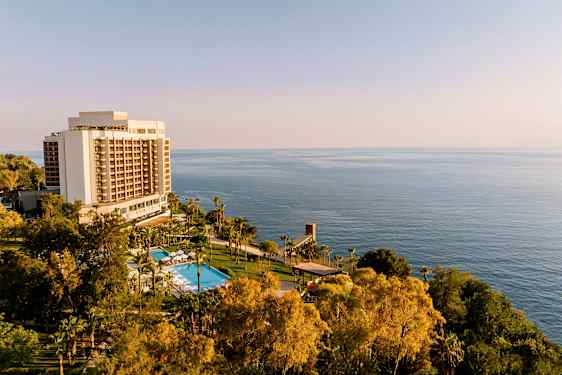 Hotellbygning med basseng og grønne områder foran havet. (AI-generert tekst)