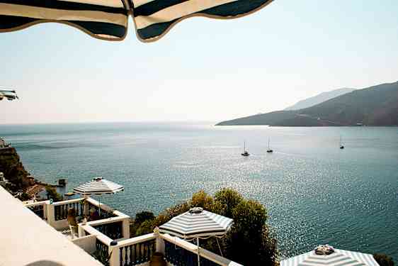 Bilde av havutsikt med solrefleksjoner, seilbåter og terrasse med parasoller. (AI-generert tekst)