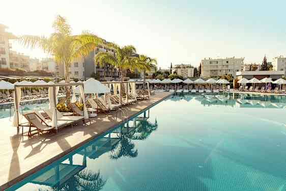 Et svømmebasseng med solsenger og parasoller i en feriestedmiljø. (AI-generert tekst)