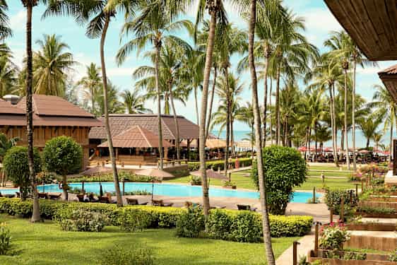 Bilde av en tropisk ferieresort med et basseng omgitt av gressplen, palmer og bygninger. (AI-generert tekst)