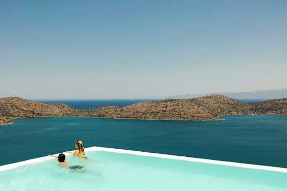 To personer i et infinity-basseng med utsikt over havet og fjell i bakgrunnen. (AI-generert tekst)