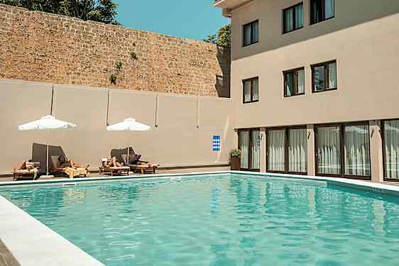 Utendørs basseng med solsenger og parasoller ved en bygning. (AI-generert tekst)