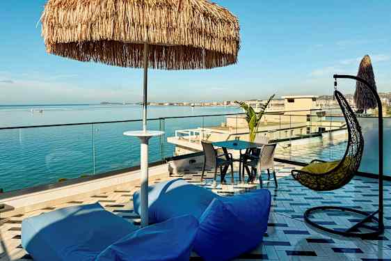 En takterrasse med utsikt over havet, med sitteplasser, en parasoll og en hengestol. (AI-generert tekst)