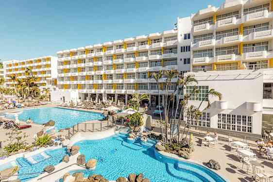 Hotellbygning med solsenger og bassengområde. (AI-generert tekst)