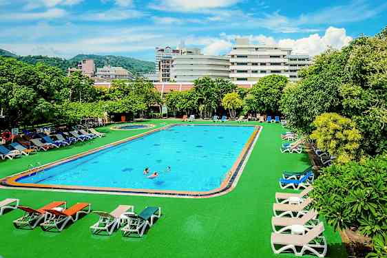 Utendørsbasseng med solsenger rundt, omgitt av grøntområder og bygninger i bakgrunnen. (AI-generert tekst)