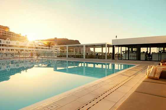 Utendørs svømmebasseng ved et hotell med solsenger og en bygning i bakgrunnen. (AI-generert tekst)