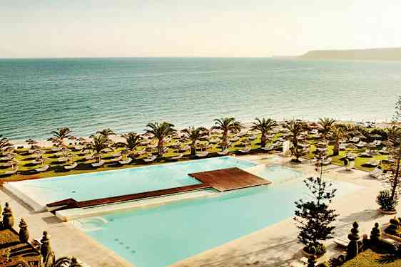 Utsikt over et svømmebasseng, solsenger og plenområder, med havet i bakgrunnen. (AI-generert tekst)