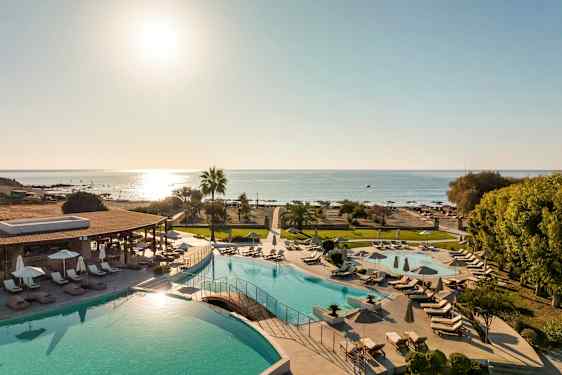 Utsikt over et bassengområde med solsenger og parasoller, samt stranden og havet i bakgrunnen. (AI-generert tekst)