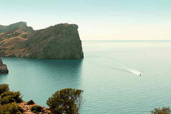 En klippe ved en kyst med en båt som kjører på vannet. (AI-generert tekst)