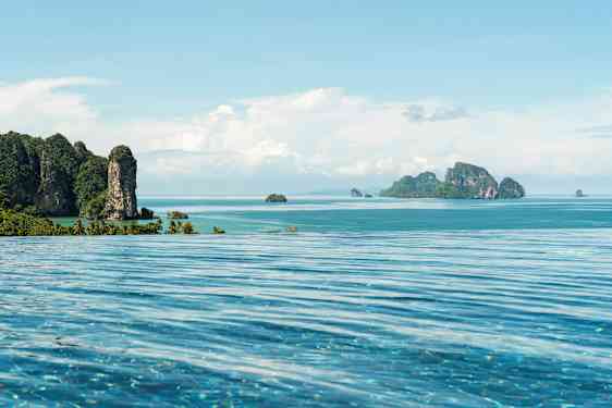 Et evighetsbasseng i forgrunnen med utsikt over en tropisk kyst- og havutsikt med fjellrike øyer. (AI-generert tekst)