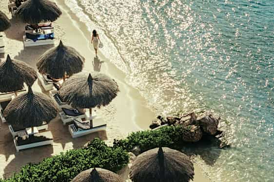 En sandstrand med parasoller og solsenger ved siden av et klart hav. (AI-generert tekst)