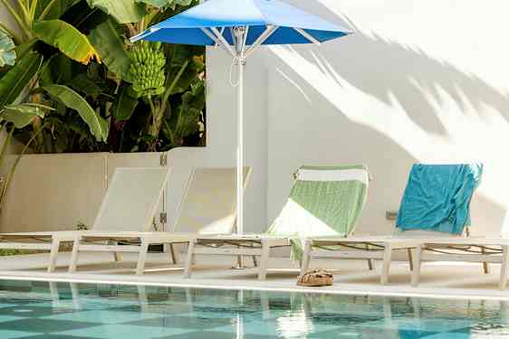 Solstoler og parasoll ved bassenget, med bananplanter i bakgrunnen. (AI-generert tekst)