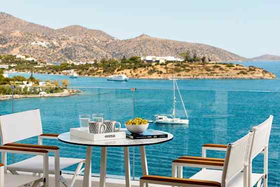 En terrasse med bord og stoler med utsikt over havet og en øy. (AI-generert tekst)