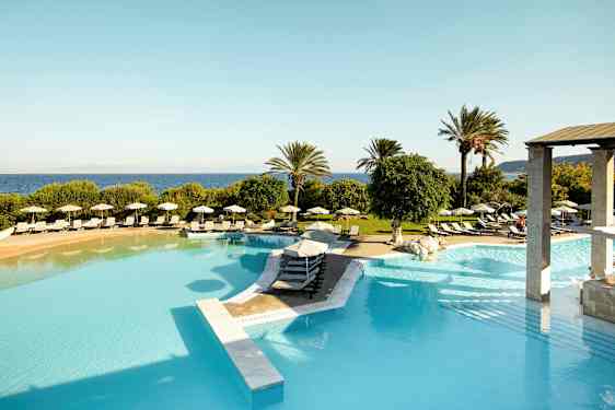 Bilde av et stort utendørsbasseng med solsenger og parasoller rundt, omgitt av frodighet og palmetrær med havet i bakgrunnen. (AI-generert tekst)