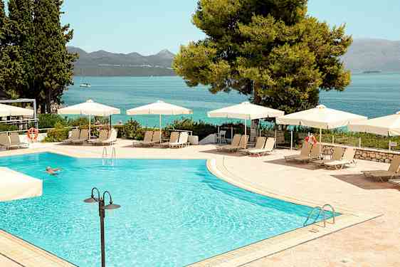 Utendørs basseng med parasoller og solsenger, i bakgrunnen sees havet og fjellene. (AI-generert tekst)