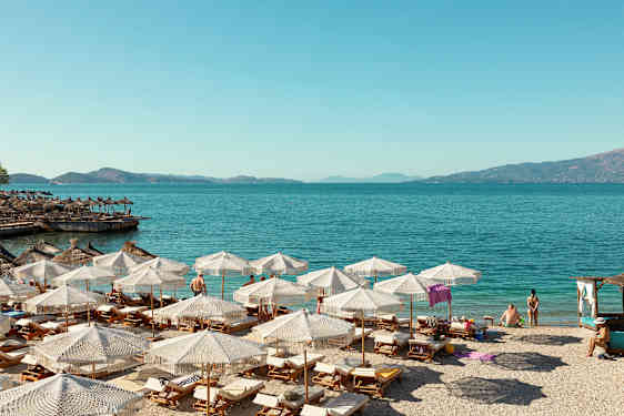 Strand med solsenger og parasoller ved klart blått vann. (AI-generert tekst)