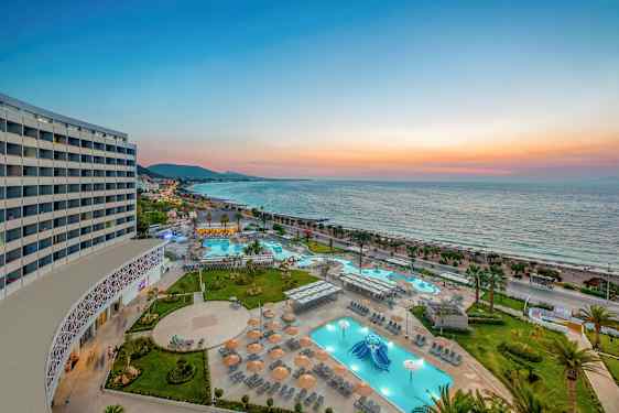 Bilde av et feriested med bassenger og solsenger ved havet under solnedgang. (AI-generert tekst)