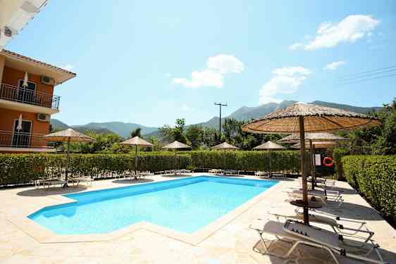 Utendørsbasseng omgitt av solsenger og parasoller, med vegetasjon og fjell i bakgrunnen. (AI-generert tekst)