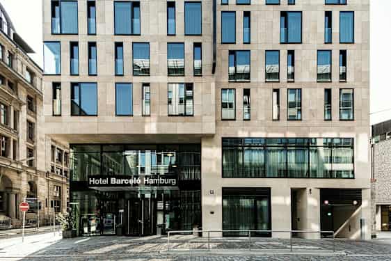 Et bygg med en moderne fasade og en inngang hvor det står "Hotel Barceló Hamburg". (AI-generert tekst)