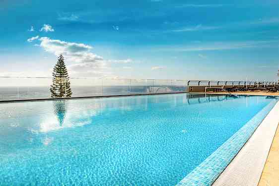 Takbasseng med klart blått vann og utsikt mot himmel og tre. (AI-generert tekst)