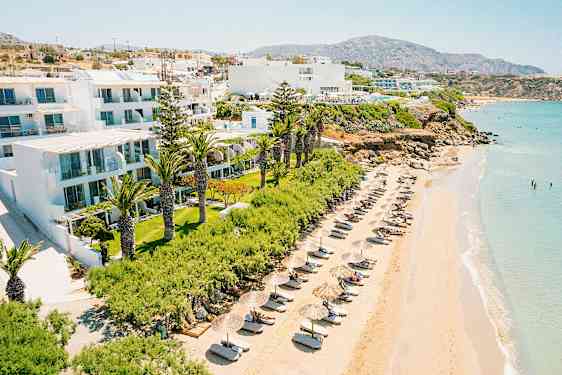 Strand med solsenger og parasoller ved en hotellbygning omgitt av grøntområder. (AI-generert tekst)