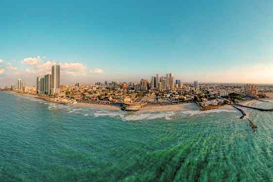Panoramabilde av en kystby med høye bygninger, strand og hav. (AI-generert tekst)