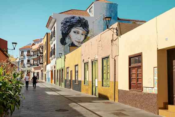 Fargerike husfasader langs en gangvei med to personer som går. (AI-generert tekst)