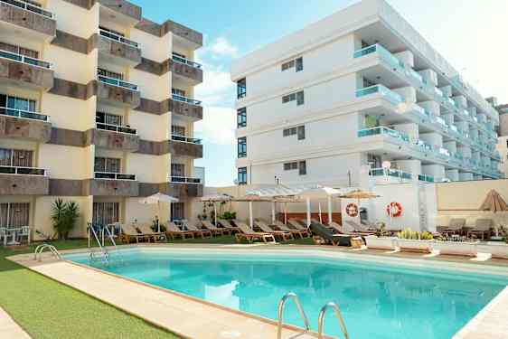 Hotellbygninger ved et utendørsbasseng omgitt av solsenger og parasoller. (AI-generert tekst)