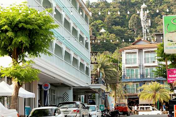 Gatebilde med parkerte biler, en bygning med blå fasade og frodige trær. (AI-generert tekst)