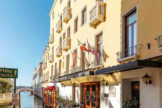 En gul bygning med balkonger langs en kanal, med en gangbro i bakgrunnen. (AI-generert tekst)