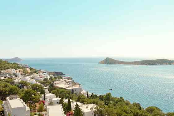 Utsikt over kystlinje med hvite bygninger og grønne trær, havet og en øy i bakgrunnen. (AI-generert tekst)
