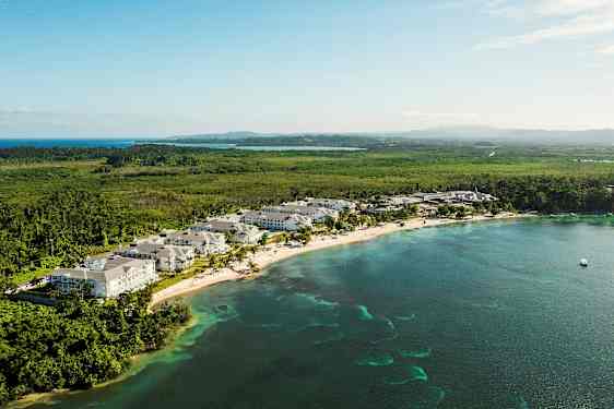 Utsikt over en kystlinje med ferieanlegg, omgitt av grøntområder og hav. (AI-generert tekst)