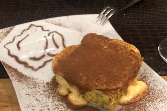 Tiramisu servert på en firkantet tallerken med et dryss kakao og krem som renner ut på sidene.