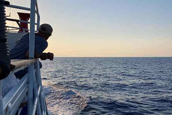 Mann som lener seg mot rekkverket på ferjen ute på havet ved soloppgang