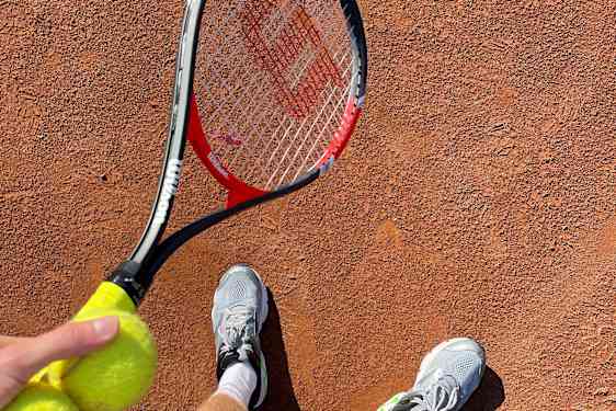 Mann holder en tennisracket og ball