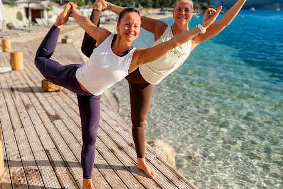 Instruktørene for yogareisen til Hellas står i yoga-posisjon med bena og armene i været