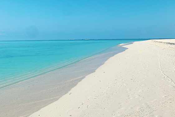 Kritthvit sandstrand med turkisblått hav og klarblå himmel