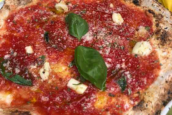 Nærbilde av pizza med tomatsaus, basilikumblader, ost og et dryss revet parmesan på en luftig pizzabunn.