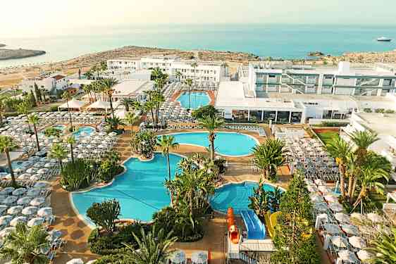 Oversiktsbilde av resort ved havet med flere bassenger, palmer, solsenger og moderne hotellbygninger. Det turkisblå havet danner en vakker bakgrunn til ferieanlegget.