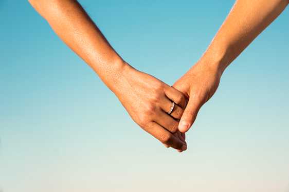 Par som holder hender i solen
