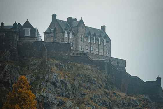 Edinburgh Castle ruver på en klippe under grå himmel, omgitt av steinmurer og høstfarger.