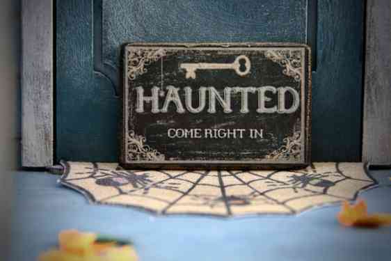Skilt med teksten «Haunted – Come Right In» står på en dørmatte med spindelvevsmønster.