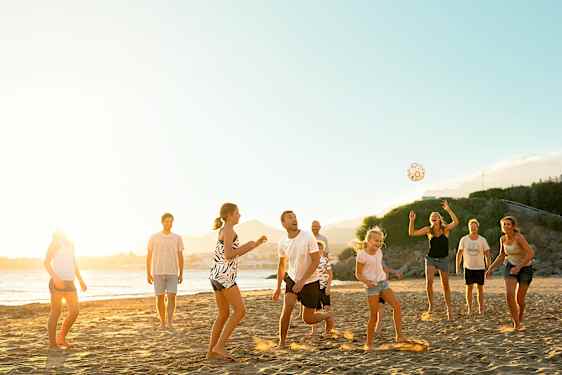 En stor gruppe mennesker spiller volleyball på stranden