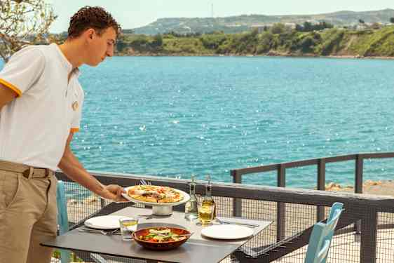 Servitør serverer mat på en terrasse, med utsikt over havet