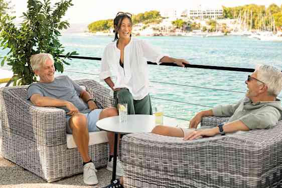 Tre personer slapper av sammen på en terrasse med utsikt over havet.